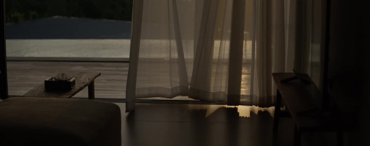 Golden sunset light reflects on the floor of a tranquil room as sheer curtains gently sway in the breeze, revealing a calm pool outside