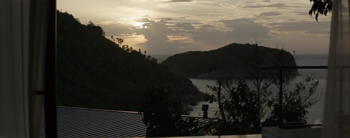 A slow pan reveals a serene sunset over a tranquil ocean cove and lush green hills