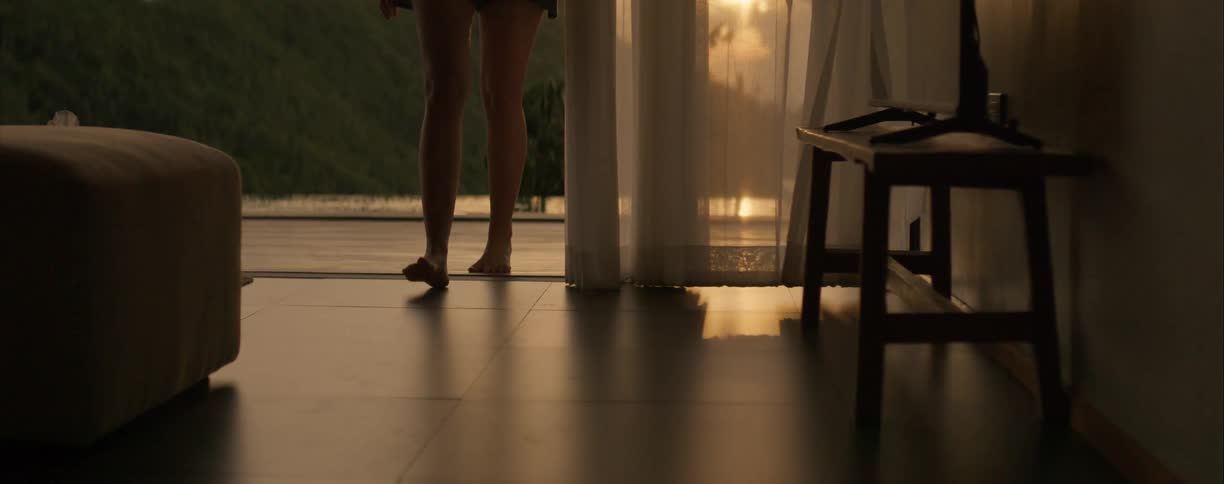 Low-angle slow-motion shot of a woman's bare feet walking across a tiled floor towards a sofa during a beautiful golden hour