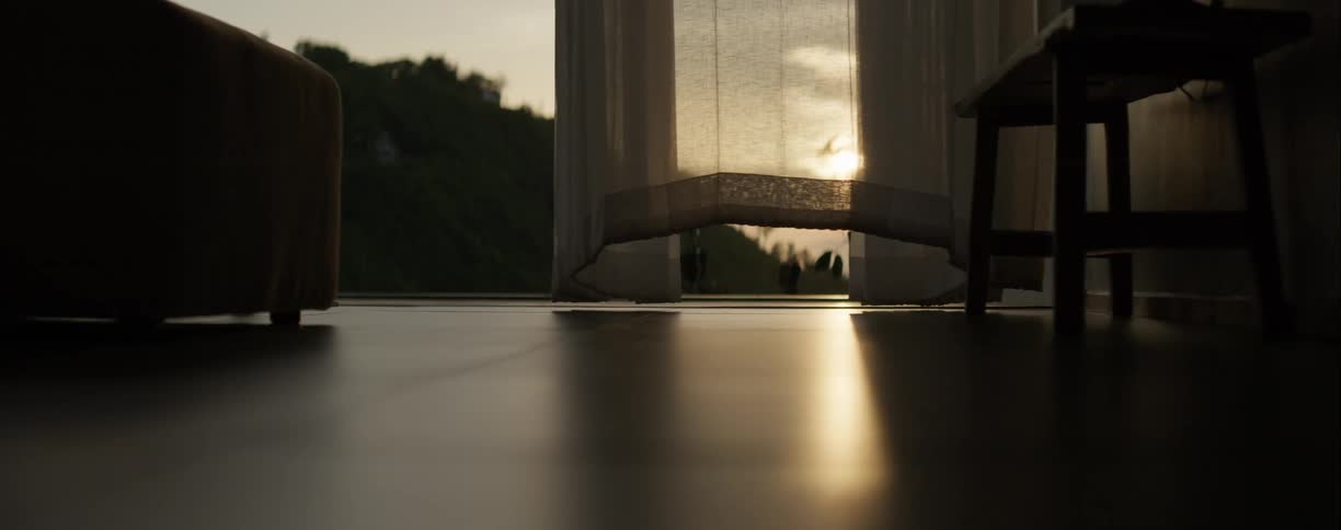 Sheer curtain gently blows in the wind revealing a beautiful sunset view from a peaceful room
