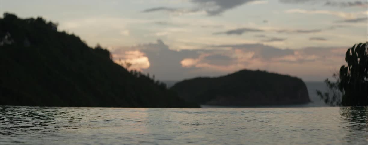 A serene view from an infinity pool of silhouetted tropical islands at sunset as the focus racks to the calm water