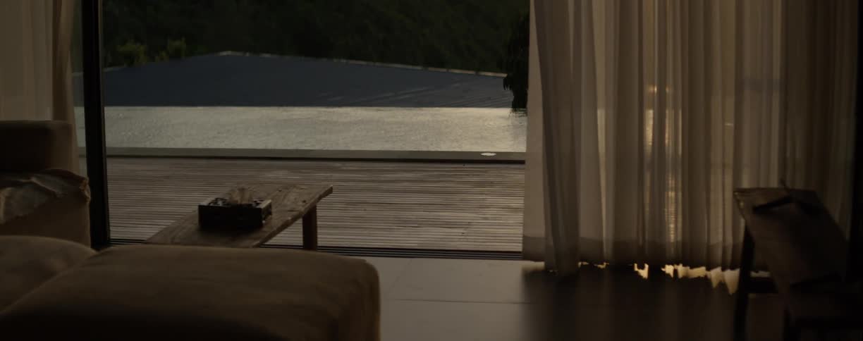 The wind gently blows through the curtains of a luxury hotel room overlooking a tranquil infinity pool at golden hour