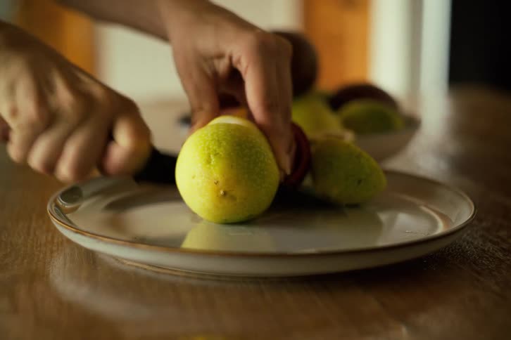 A person carefully cuts a ripe passion fruit on a ceramic plate, revealing the juicy pulp inside