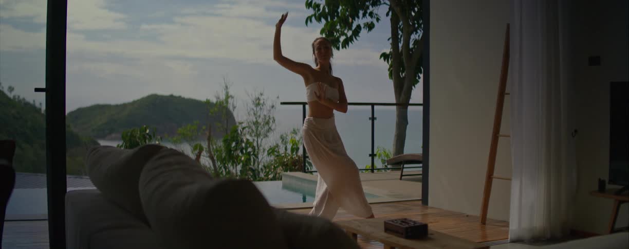 Slow motion shot of a graceful woman in white performing an expressive dance on a terrace with a pool overlooking the ocean