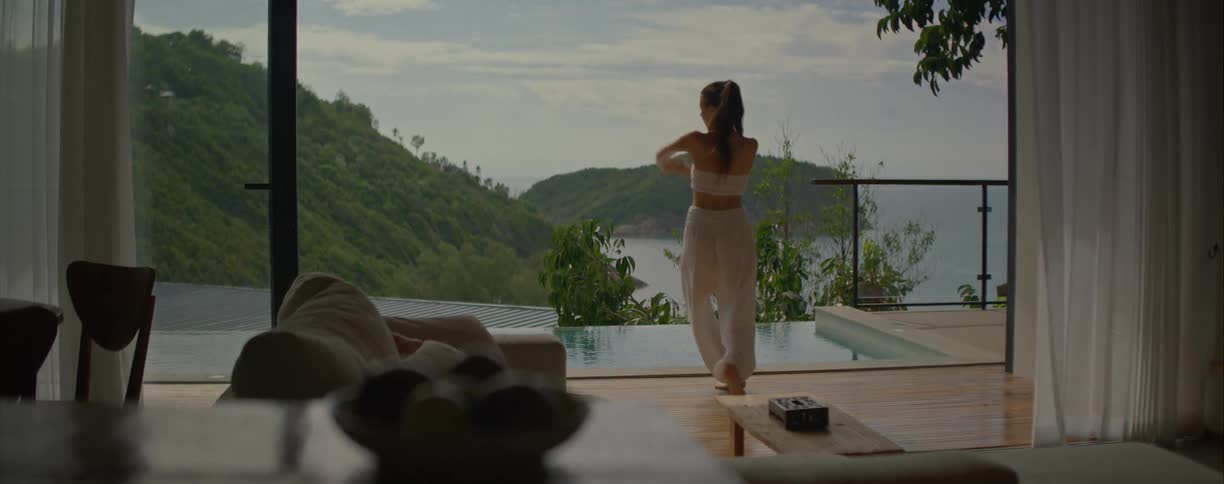 A woman in white gracefully dances by an infinity pool in a luxury villa with a breathtaking tropical sea view