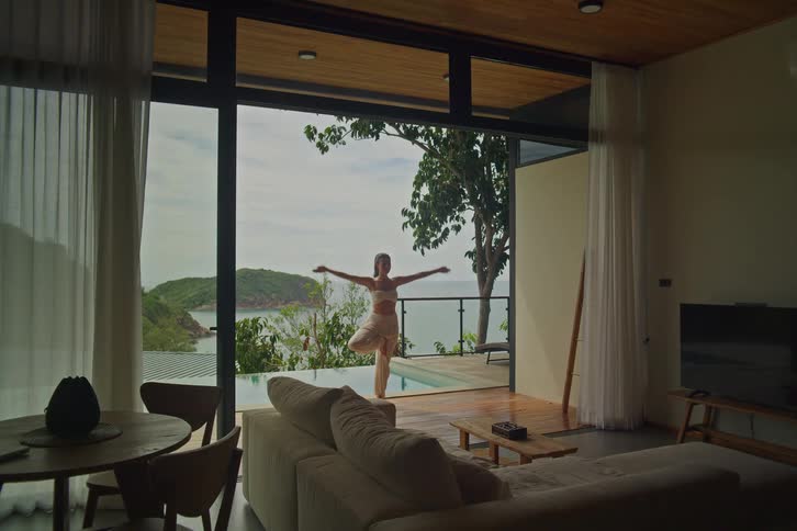 A serene woman practices the tree pose yoga on the terrace of a luxury villa overlooking the ocean