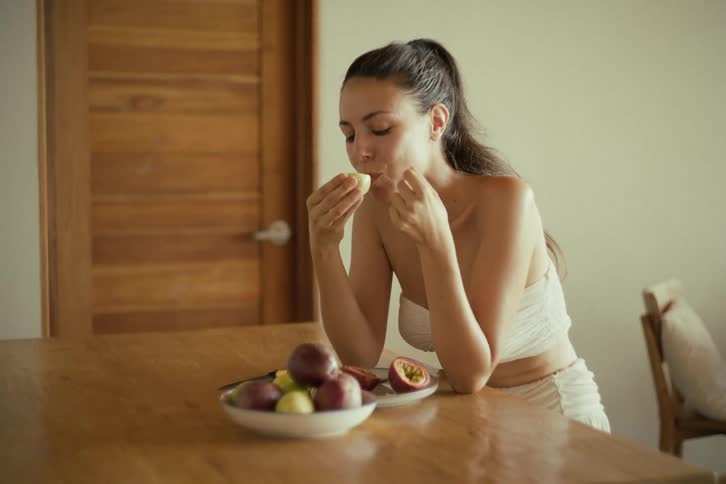 A beautiful woman in slow motion enjoys eating a fresh, ripe passion fruit for a healthy snack