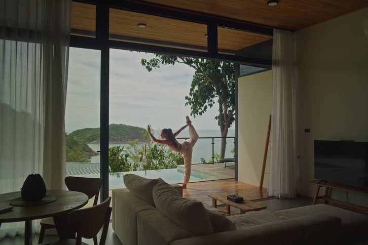 Woman practices yoga and stretches on the balcony of a luxurious villa with an infinity pool overlooking the ocean