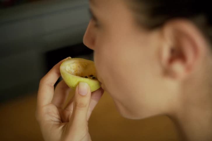 A woman enjoys the sweet taste of a fresh passion fruit, eating it with a small spoon