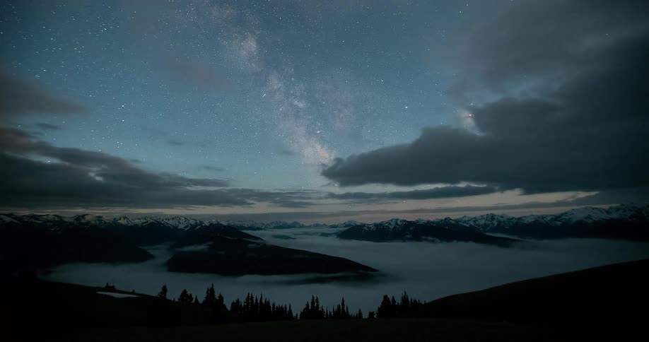 A stunning night sky time-lapse shows the Milky Way appearing over a majestic mountain range as clouds roll through the valley below