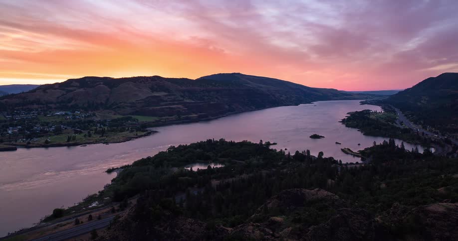 A stunning timelapse captures the vibrant pink and orange sunrise over a majestic river gorge as traffic flows along the highways below