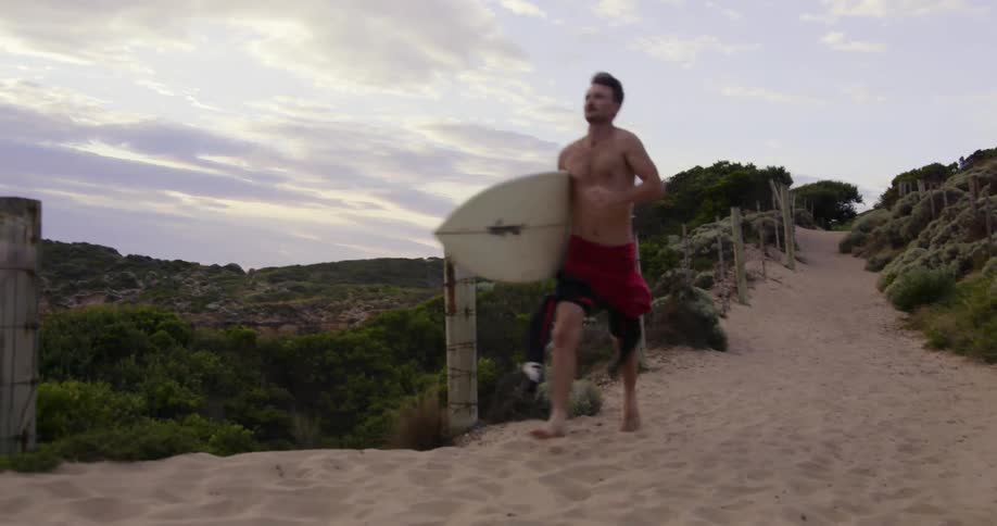 A man runs downhill with his surfboard