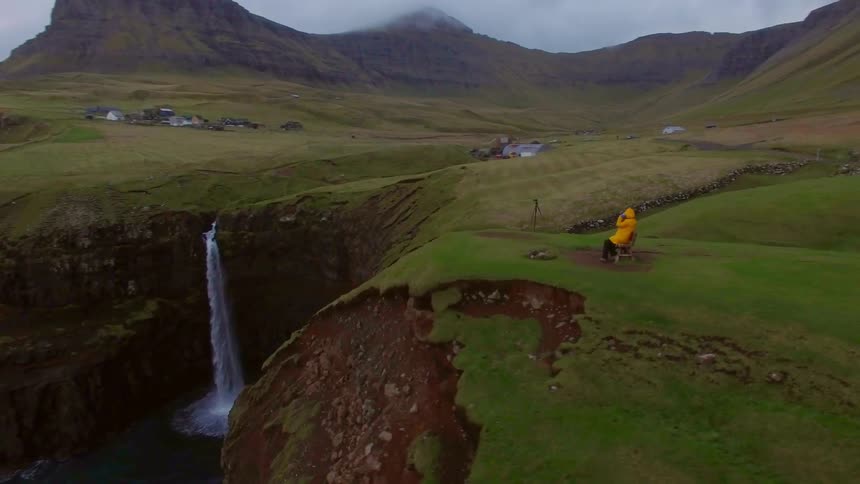 A person in a yellow raincoat sits on a cliffside bench