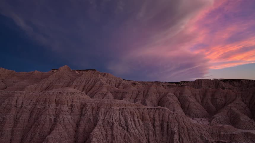 A breathtaking timelapse shows a vibrant, colorful sunset fading over the rugged rock formations of the Badlands National Park