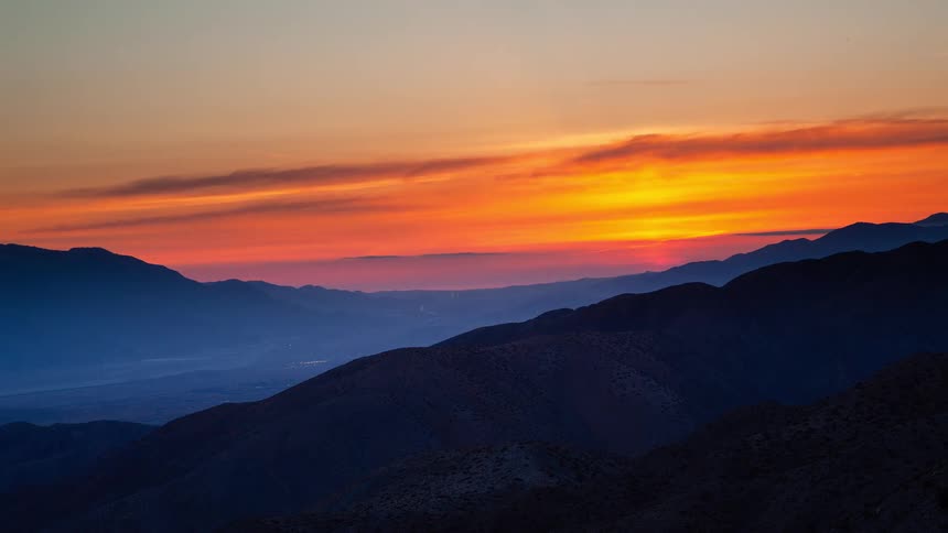 A stunning timelapse shows the sun setting in a vibrant display of orange and yellow behind a vast mountain range