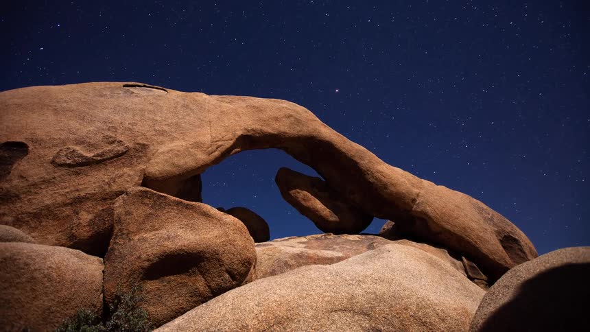 Shifting moonlight illuminates the stunning Arch Rock as stars trail across the night sky in this beautiful timelapse