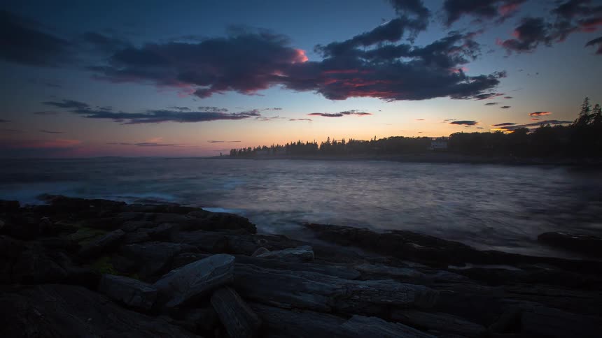 Vibrant sunset clouds fade to darkness over a rocky ocean shore in this stunning long-exposure timelapse