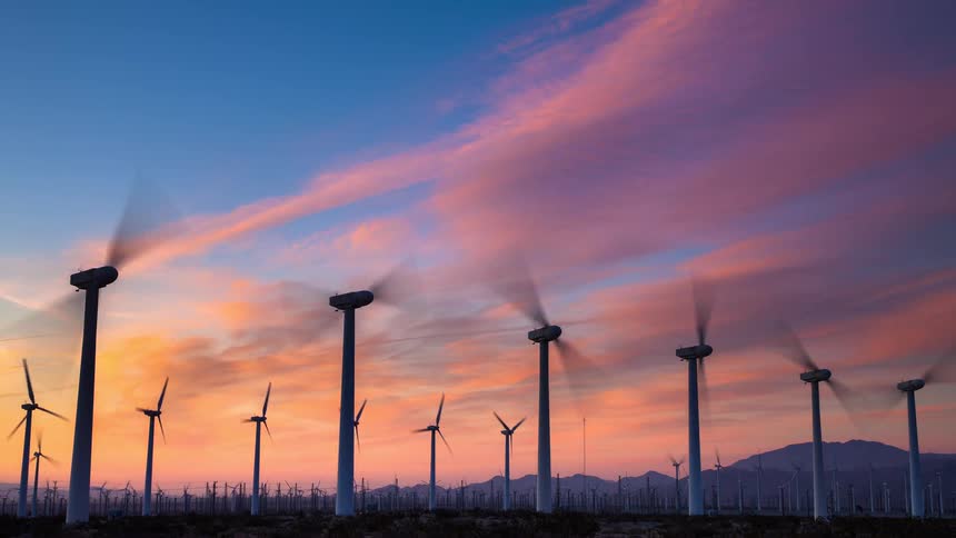 A beautiful time-lapse of numerous wind turbines spinning against a vibrant and colorful sunrise sky, generating clean, renewable energy