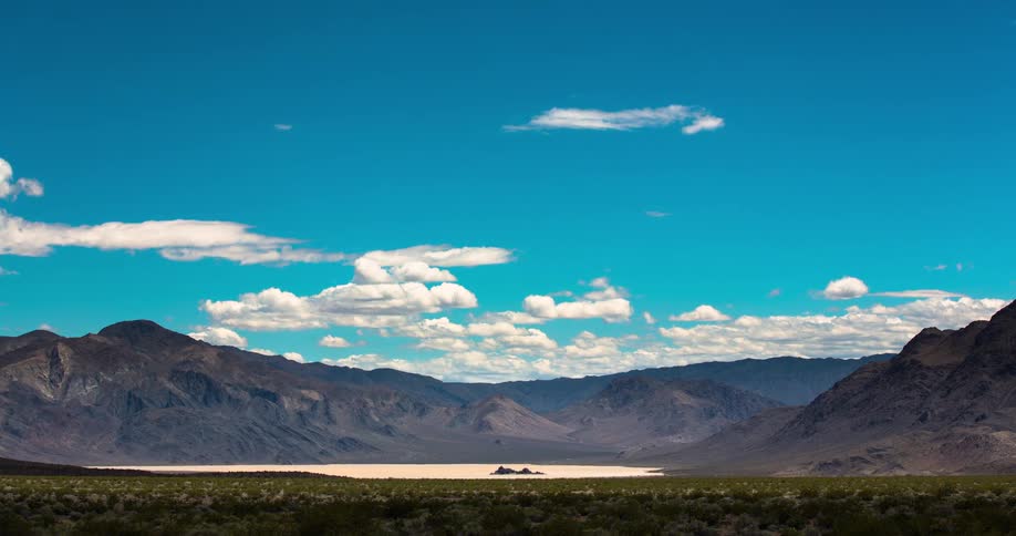 A stunning time-lapse of white clouds floating across a deep blue sky over the mountainous desert landscape of Death Valley National Park