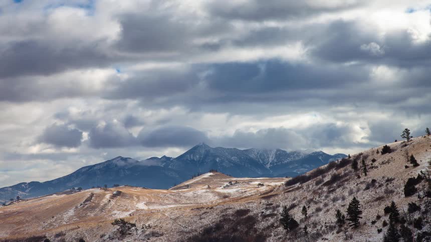Time-lapse of dramatic storm clouds moving over snow-dusted mountains and rolling hills