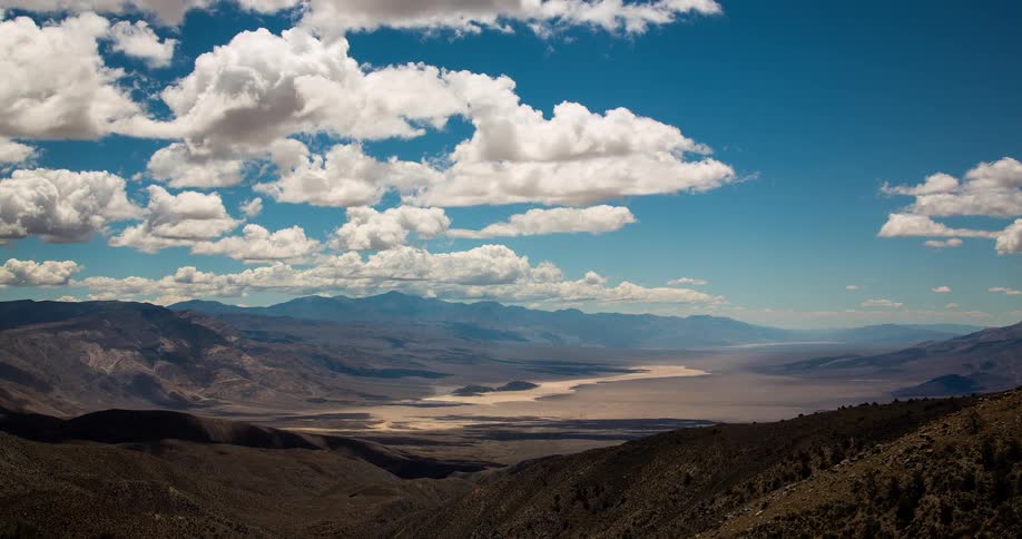 A stunning timelapse shows white clouds casting moving shadows across a vast desert valley surrounded by mountains