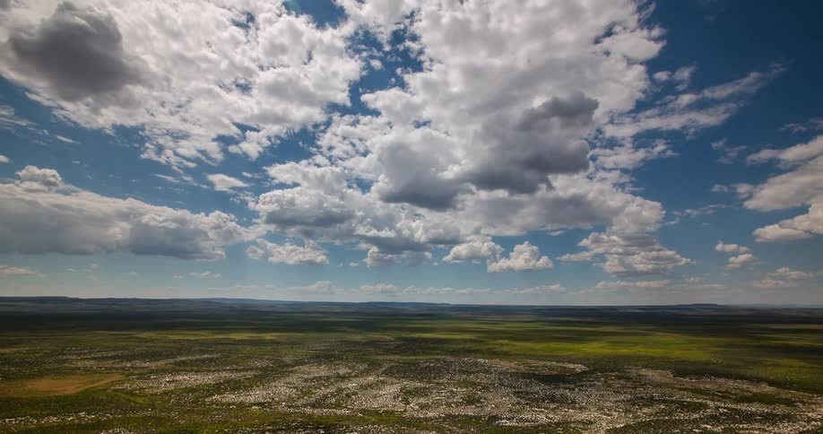 Time-lapse of clouds and shadows moving across a wide open green plain under a bright blue sky