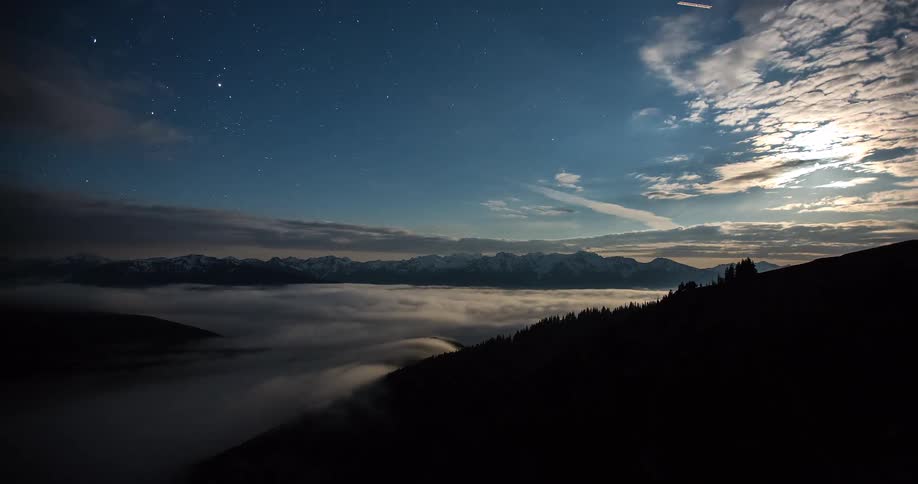 A stunning day-to-night timelapse over a mountain valley shows clouds clearing to reveal a starry night sky above a sea of fog