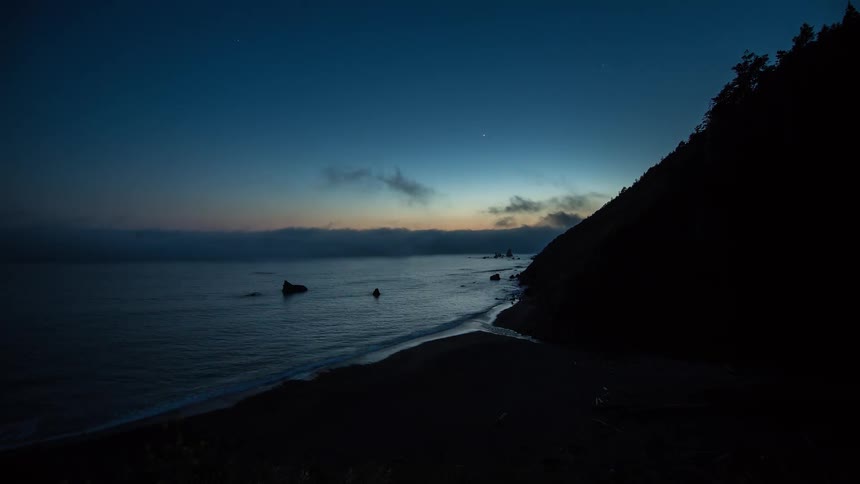 A serene timelapse of fog rolling over a secluded coastline as twilight fades into a starry night