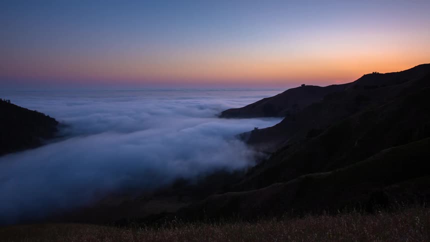 Colorful sunset timelapse over a sea of clouds flowing through a mountain valley as day turns into night