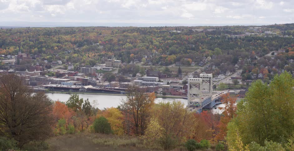 A scenic wide shot of the Portage Lake Lift Bridge connecting the towns of Houghton and Hancock, Michigan, surrounded by vibrant autumn foliage