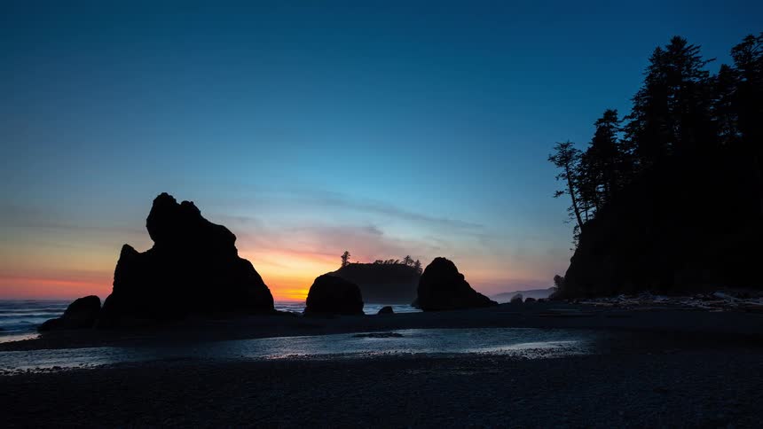A beautiful time-lapse of the sun setting behind silhouetted sea stacks on a rocky Pacific Northwest beach