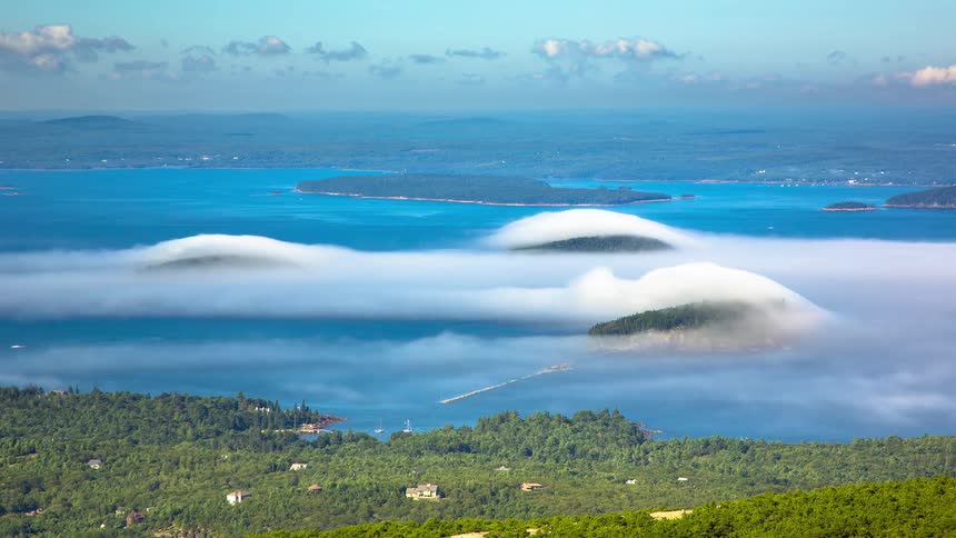 A stunning time-lapse from a high vantage point shows thick fog rolling over coastal islands surrounded by the ocean on a clear day