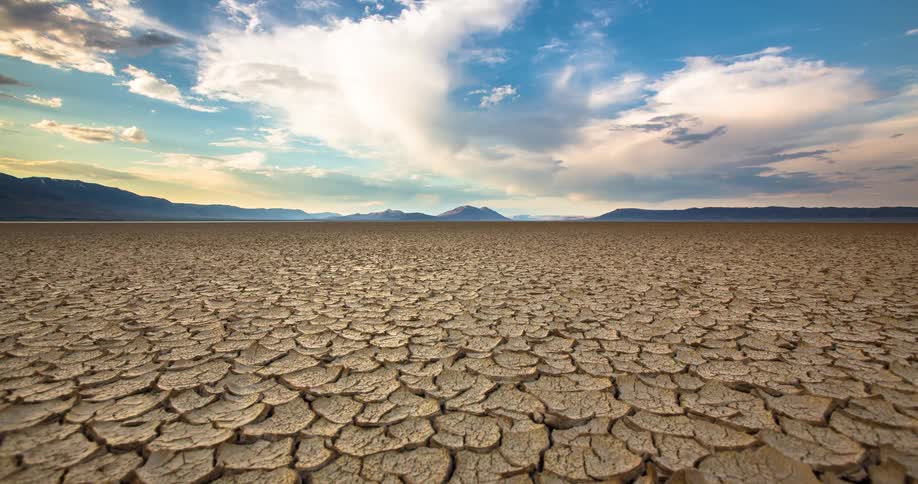 A beautiful timelapse shows clouds passing over a vast expanse of cracked, dry earth in a desolate desert landscape