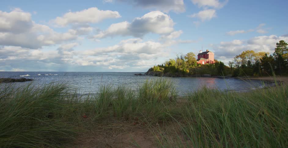 The iconic red Marquette Harbor Lighthouse overlooks the serene waters of Lake Superior from a grassy, windswept beach