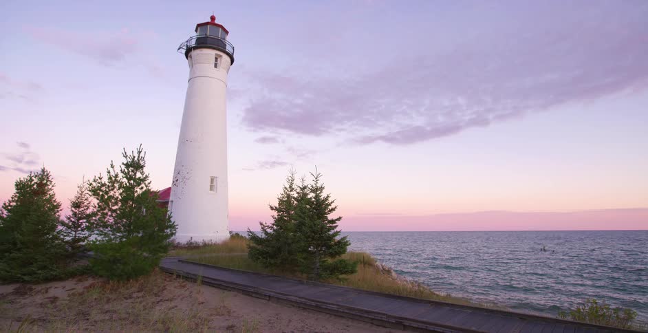 A beautiful white lighthouse stands tall on a sandy dune overlooking the water at sunset