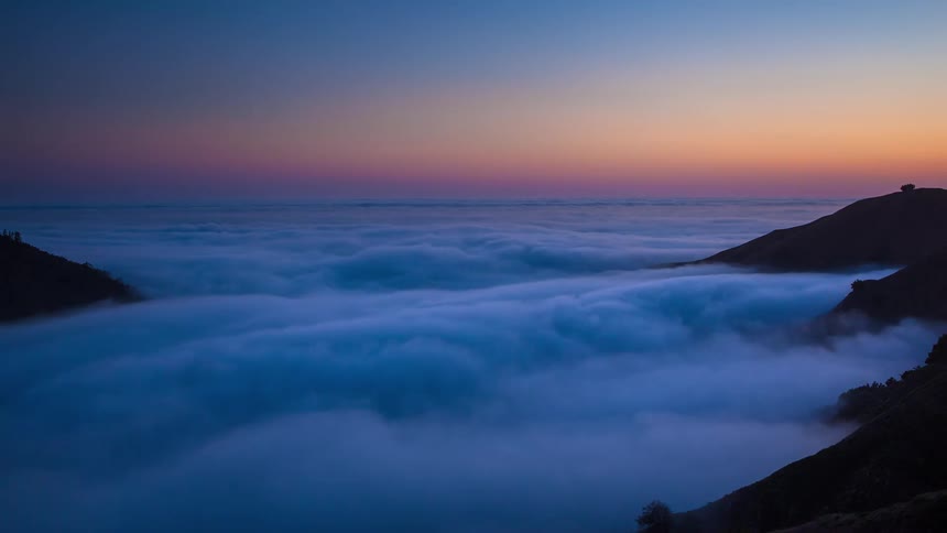 A serene timelapse of clouds flowing like a river through a mountain valley as the sun sets