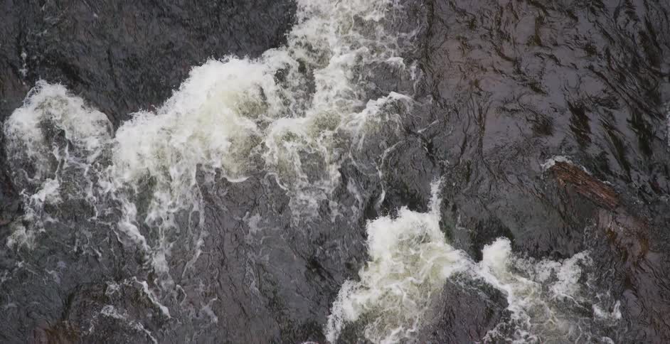 A mesmerizing slow-motion, top-down view of a powerful, churning river with turbulent rapids