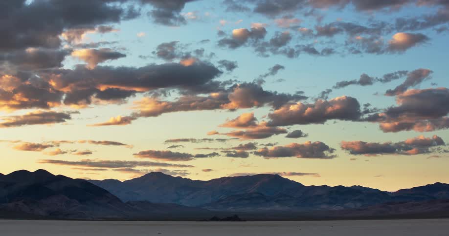 A majestic timelapse of golden hour clouds turning pink and purple as the sun sets over a desert mountain range and dry lakebed