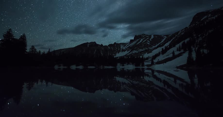 Timelapse from day to night over a snowy mountain lake as the Milky Way rises and reflects in the still water