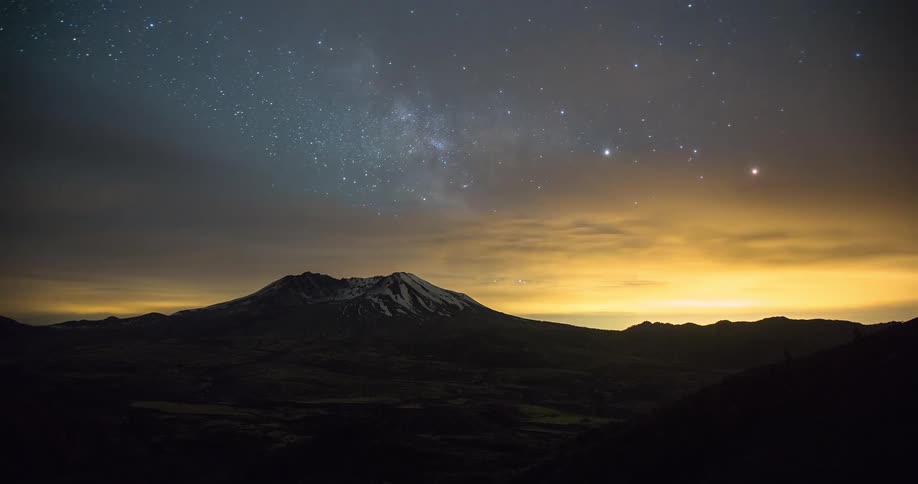 A stunning night-to-day timelapse captures the Milky Way and stars moving across the sky over a majestic snow-capped mountain, culminating in a brilliant sunrise