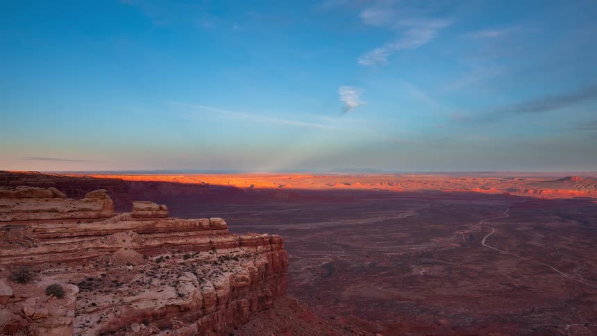 Timelapse of the sun setting over a vast desert canyon, casting a warm golden glow and long shadows before fading into twilight