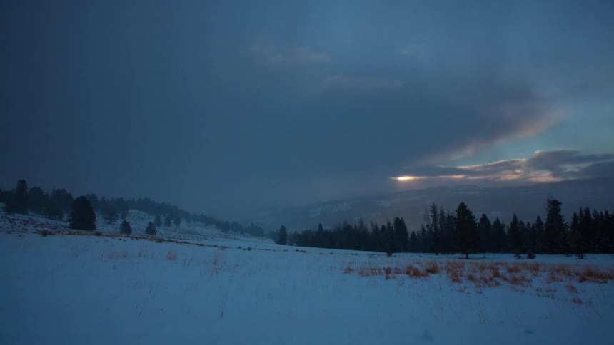A dramatic timelapse shows dark, stormy clouds giving way to a brilliant sunrise over a vast, snow-covered mountain landscape