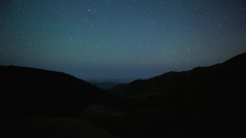 A breathtaking night-to-day time-lapse captures stars wheeling over a coastal valley filled with a sea of fog, transitioning to a bright, sun-filled morning