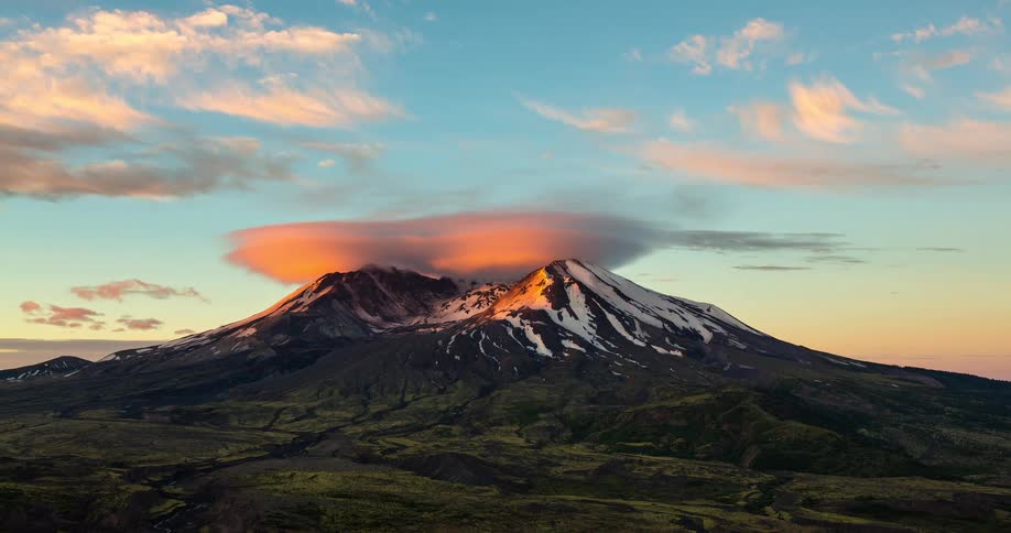 A stunning timelapse shows a lenticular cloud over a snow-capped mountain as the sky transitions from dusk to a vibrant, colorful sunrise