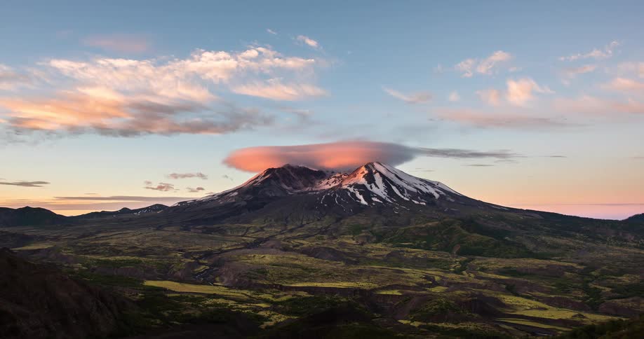 Dramatic sunrise timelapse over a snow-capped volcano with a prominent lenticular cloud glowing in the morning light
