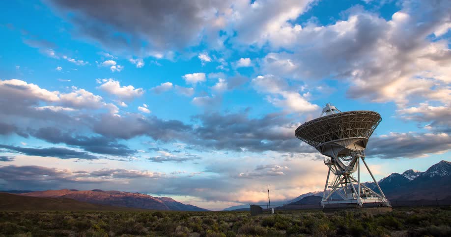 A timelapse of a large radio telescope in a desert valley as dramatic storm clouds pass and the sun sets