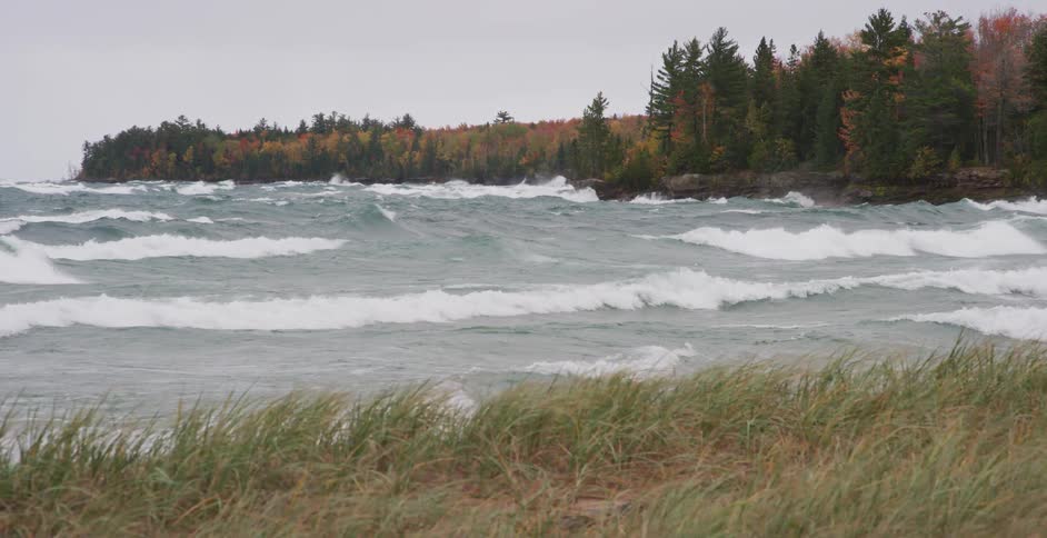 Slow motion footage of large, turbulent waves crashing against a rocky, forested shoreline during an autumn storm
