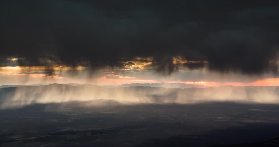 A dramatic time-lapse captures a powerful thunderstorm with heavy rain and lightning pouring over a mountain valley at sunset