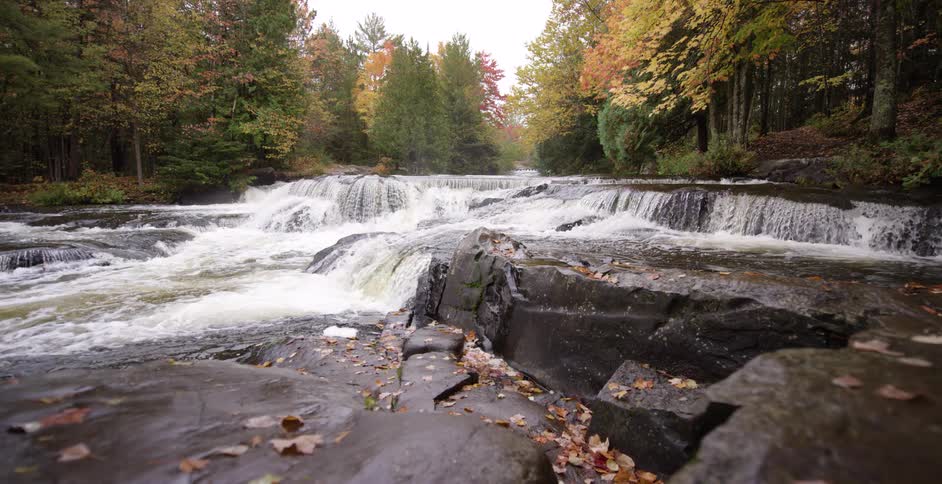 A beautiful wide waterfall cascades over rocks in a forest during the peak of autumn colors