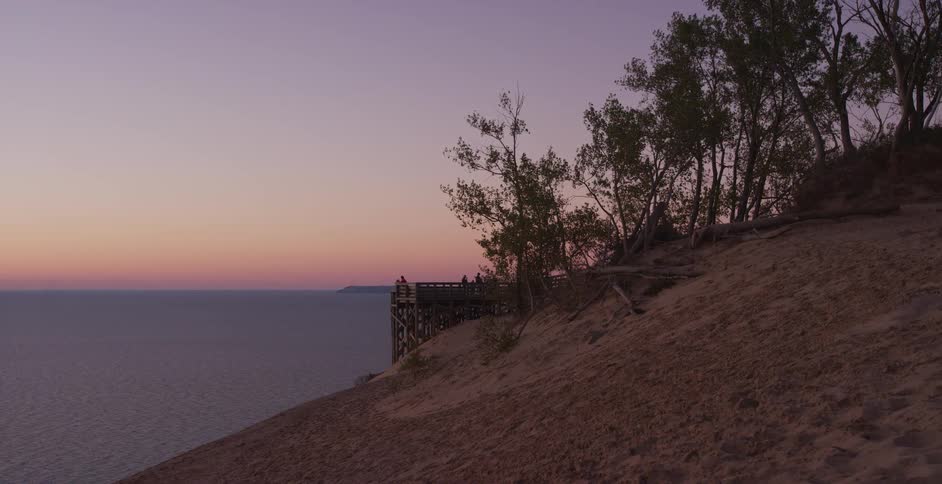 A serene sunset view from a sandy dune with a wooden observation deck overlooking the calm ocean